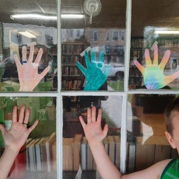 Wabeno Public Library window with three handmade paper hands colored and taped to the panes.